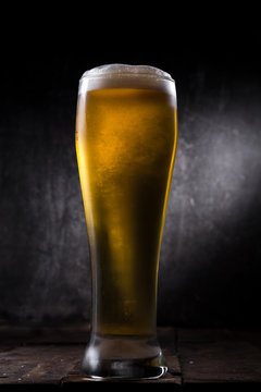 Cold beer glass with condensation and bubbles over grey concrete background