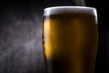 Cold beer glass with condensation and bubbles over grey concrete background