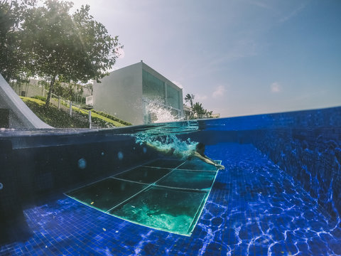 split shot of a young woman diving into a pool beside a luxurious villa