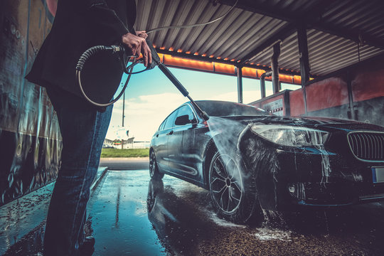 Smart trendy man in jeans and blaser is washing his own car at car washing station.