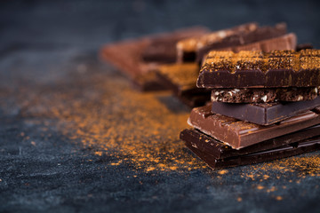 Broken chocolate stacked on black background. Chocolate bar pieces heap witn cinnamon powder.