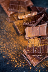 Broken chocolate stacked on black background. Chocolate bar pieces heap witn cinnamon powder.