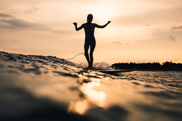 Young woman surfing waves in the ocean at sunset