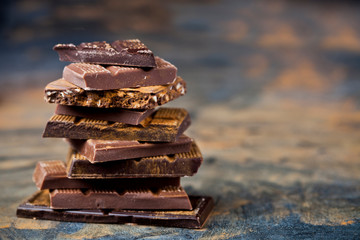 Broken chocolate stacked on black background. Chocolate bar pieces heap witn cinnamon powder.
