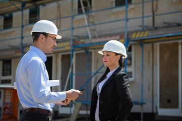 Two architects a man and a woman in construction in white helmets.