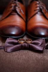 gold wedding rings lie on the table next to the men's bow tie and shoes