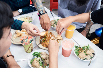 From above crop of four unrecognizable male hands eating asian street food.