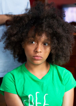 Portrait of a pretty teenage girl sitting as her sister helps her comb her kinky curly hair