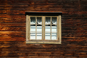 A detail of the planks of the scandinavian wooden house. The color of the house is old and looks shabby. One window can be seen. 