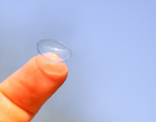 Transparent contact lens on finger tip on blurred summer nature background