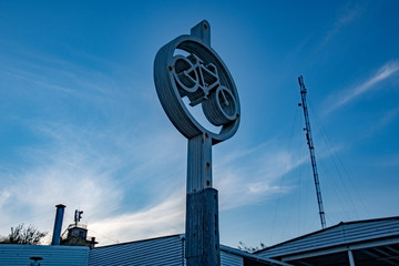 Silhouette of bike parking road sign on dusky blue sky background. Bicycle parking sign cutout from layered plywood. Outdoor scene in blue monochrome shades.  Cloudscape with white spindrift clouds