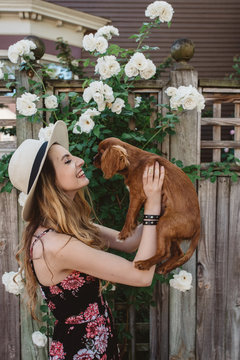 A woman in her twenties walking her puppy down the street in the summer time.