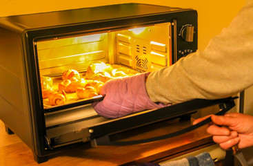 Woman checks the process of homemade sweet cinnamon roll baking on a sheet in oven