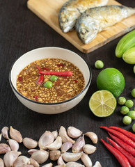 Chili paste (thai language Nam prik kapi) in a white bowl with ingredients and Fried steam mackerel on the table.
