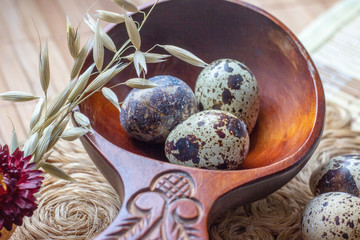 Fresh raw quail eggs in wooden spoon on rustic straw and wooden vintage background