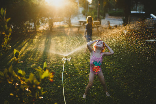 Girl in swimsuit playing on grass with sprinkler