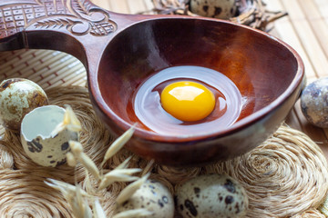 Fresh raw quail eggs in wooden spoon on rustic straw and wooden vintage background