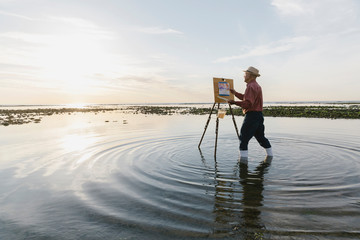 En plein air painter painting in sea with easel