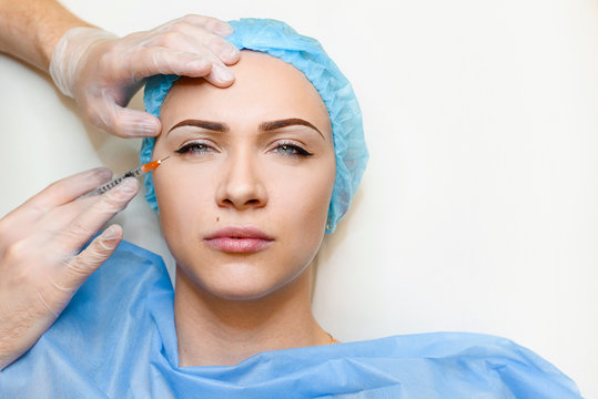 Woman makes botox injections in eye corner. Doctor cleans the girl's face from wrinkles. Clear crows feet by botox injections. Plastic surgery in private medical clinic.