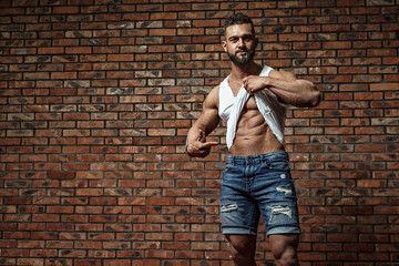 Fototapeta na wymiar Portrait of strong healthy handsome Athletic Man Fitness Model posing near Brick wall