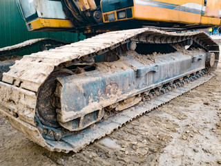 Closeup image of excavator tracks covered in dirt on the construction site