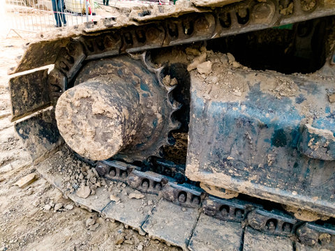 Closeup image of excavator tracks covered in dirt on the construction site