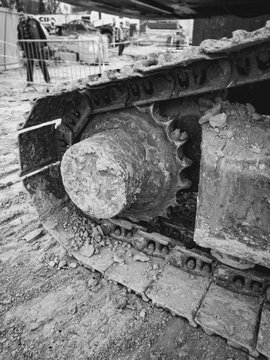 Closeup black and white image of excavator metal tracks and gears covered in mud on the building site