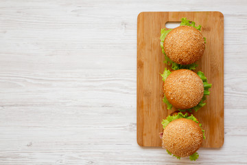 Homemade cheeseburgers on a bamboo board over white wooden background, overhead view. Flat lay, from above, top view. Copy space.