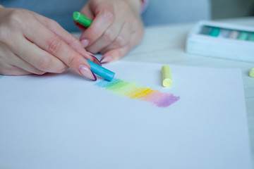 Close-up of female hands are drawing with multicolored chalks on a white sheet, a box with crayons