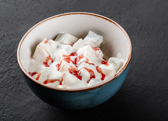 Fruit salad with banana, orange, grapes and pomegranate with cream sauce in bowl over dark background. Healthy breakfast.