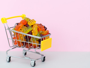 sweet and tasty pastry - gummy bears, jelly candies, in the food basket, shopping trolley on a pink-gray background with space for text. horizontal frame