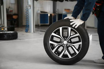 Technician rolling car wheel in automobile repair shop closeup. Space for text © New Africa