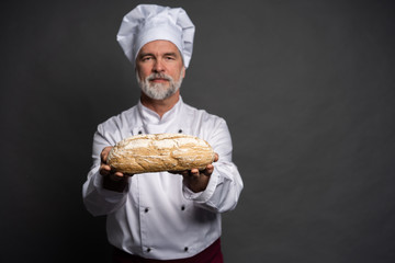 Male baker holding bread loaf and looking at camera isolated on black.