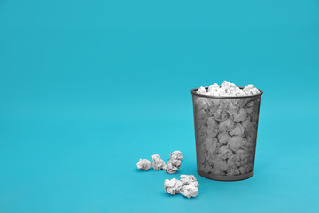 Metal bin with crumpled paper on color background, space for text