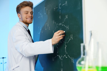 Male scientist writing chemical formula on chalkboard indoors