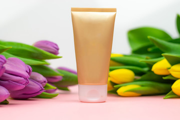 A gold tube placed on pink paper at the flowers. Ideal banner with a space for copy.