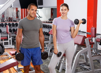 Sporty guy and girl posing with dumbbells