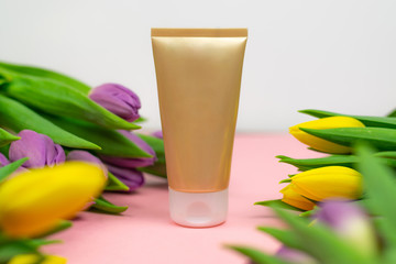 A gold tube placed on pink paper at the flowers. Ideal banner with a space for copy.