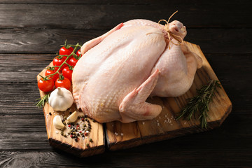 Board with raw turkey and ingredients on wooden background