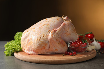 Wooden board with raw spiced turkey and ingredients on table