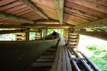 Old authentic traditional peasant wooden boat inside, under the roof of a 19th century wooden shed on Seurasaari island in Helsinki in Finland on a sunny summer day.