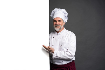 Portrait of a happy mature chef cook showing copyspace on the palms isolated on black background. - obrazy, fototapety, plakaty