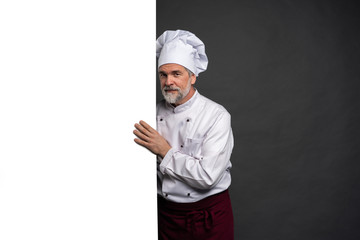 Portrait of a happy mature chef cook showing copyspace on the palms isolated on black background.
