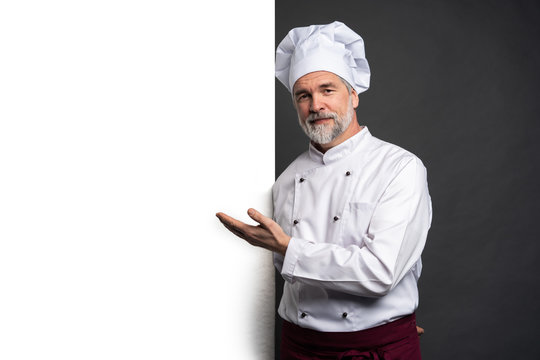 Portrait of a happy mature chef cook showing copyspace on the palms isolated on black background.