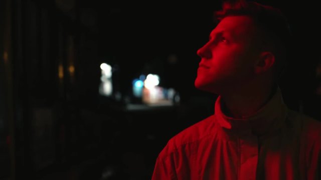 depressed young man standing on the dark street at night and looking on the red neon lamp 