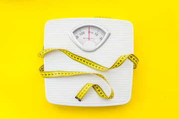 Fototapeta bathroom scales and measuring tape for weight loss concept on yellow background top view obraz