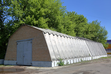 Industrial hangar with aluminum walls and roof stands on a concrete foundation near green trees