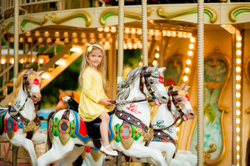 Fototapeta na wymiar Adorable little girl near the carousel outdoors in Paris, baby girl on the carousel, Happy healthy baby child having fun outdoors on sunny day. Family weekend or vacations