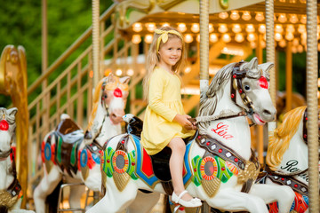 Adorable little girl near the carousel outdoors in Paris, baby girl on the carousel, Happy healthy baby child having fun outdoors on sunny day. Family weekend or vacations
