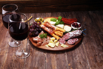 antipasto various appetizer. Cutting board with prosciutto, salami, cheese, bread and olives on dark wooden background
